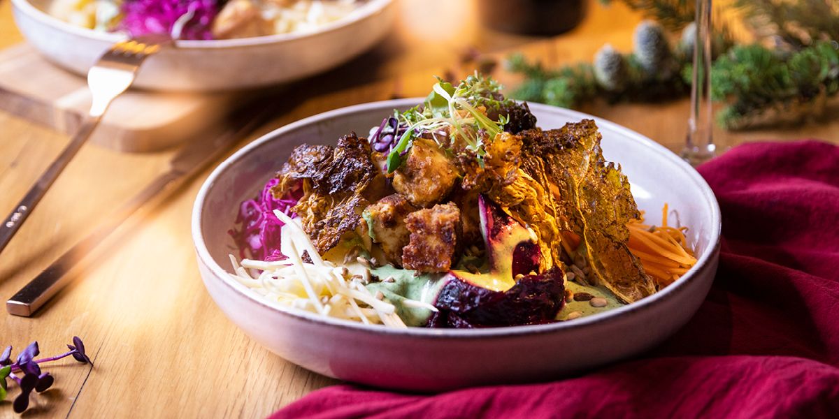 Eine Portion Vegane Winterbowl angerichtet in leicht tiefen Tellern auf einem festlich gedecketem Tisch: Auf dem Teller ist das Gemüse mit dem gebratenen Tofu angerichtet, getoppt mit Kresse.